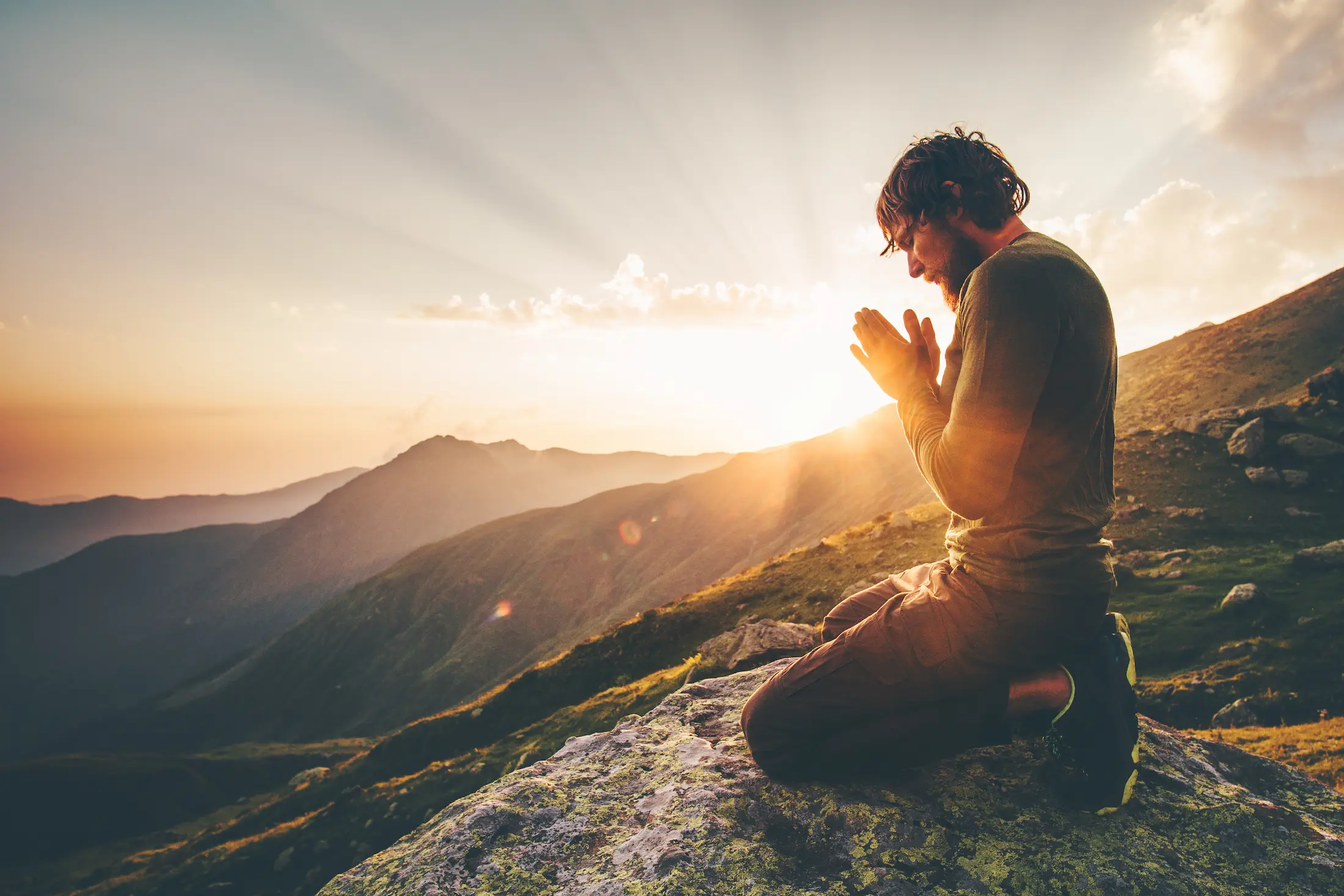 A person kneeling in prayer on a hillside at sunrise
